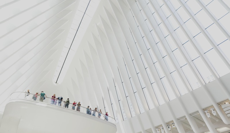 Small figures follow a balcony below sweeping white architectural ribs.
