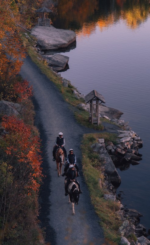 Riders follow a lakeside path below autumn trees at Mohonk in the morning.