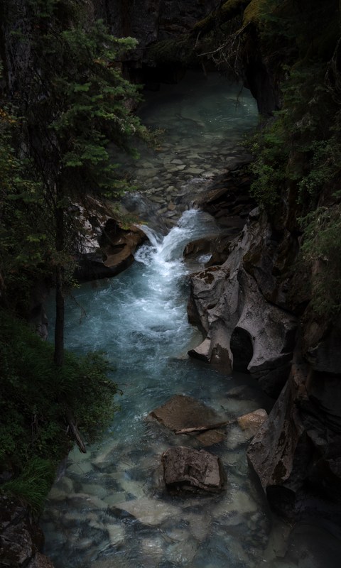 A narrow river passes through pale rock and a dark forested gorge.